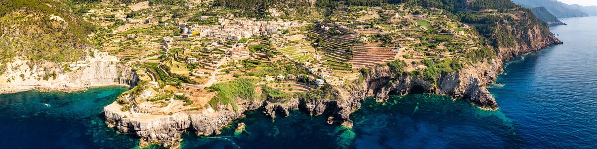 A coastal town with terraced fields, a mountain, and clear blue waters.