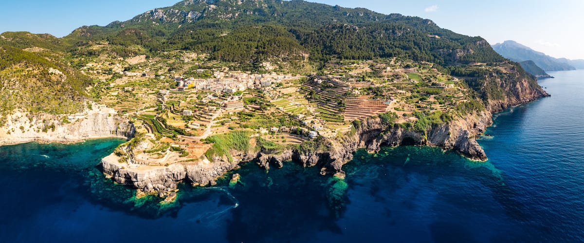 Un borgo costiero con terrazzamenti coltivati, una montagna e acque cristalline.