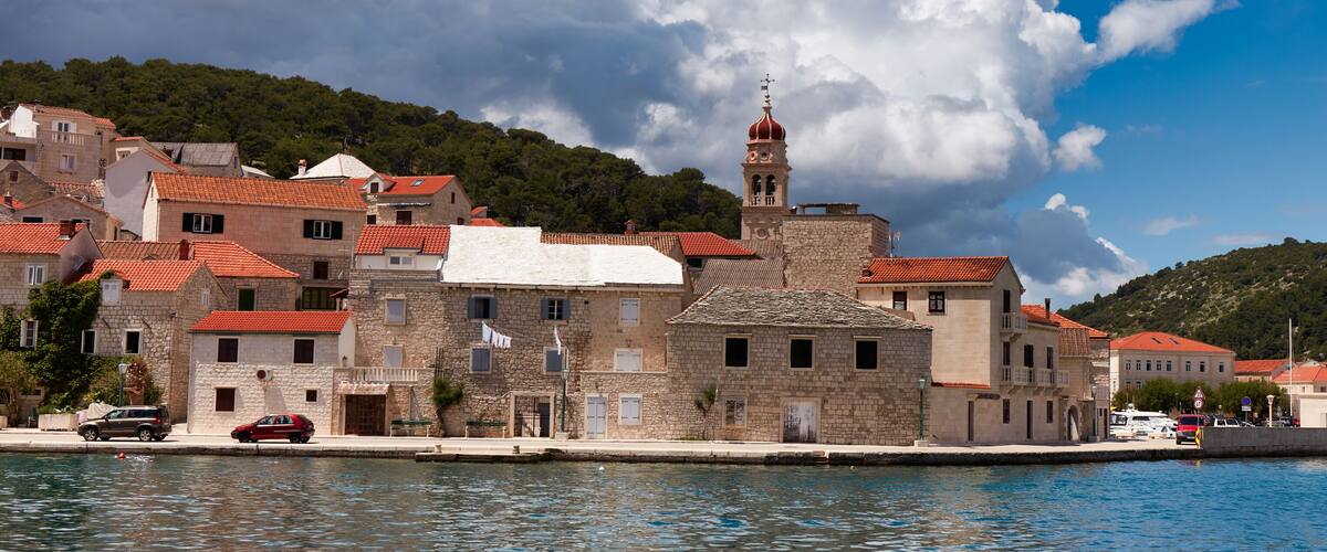 A coastal town with stone buildings, a prominent church tower, and a calm sea.