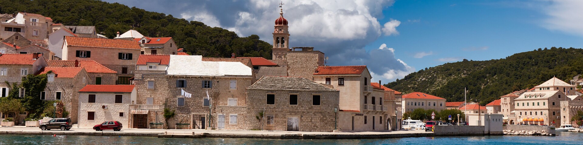 A coastal town with stone buildings, a prominent church tower, and a calm sea.