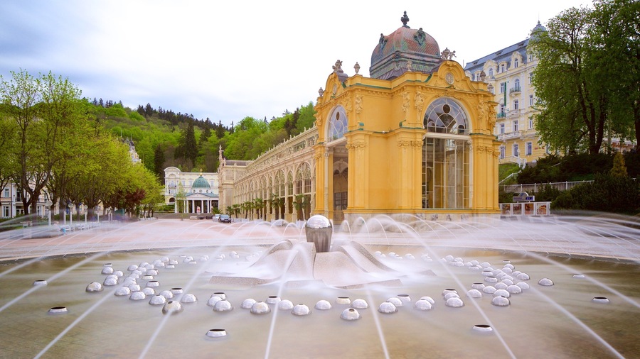 Una fuente con chorros de agua frente a un edificio amarillo de arquitectura ornamentada.