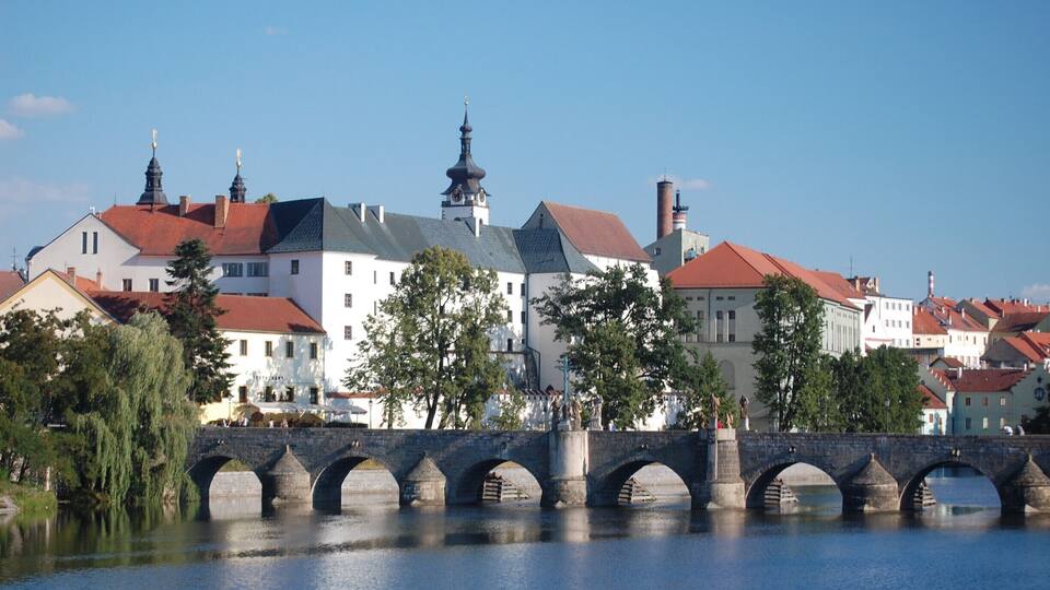 A stone bridge over a river, surrounded by historic buildings with red roofs and spires.