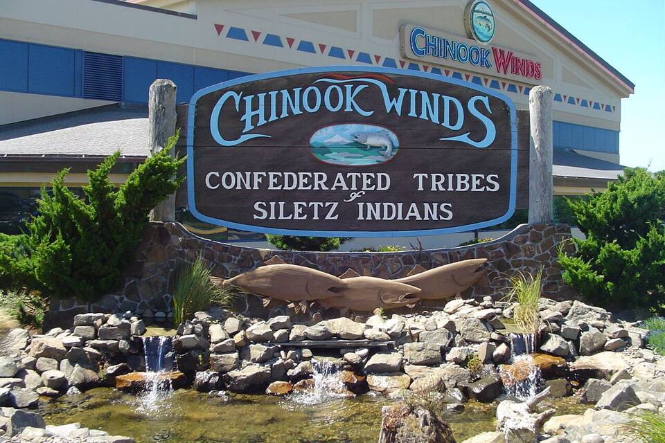 Letrero de Chinook Winds con una cascada y formaciones rocosas al frente.