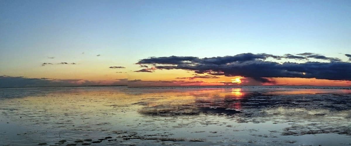 A sunset over a beach with clouds reflecting on the wet sand.