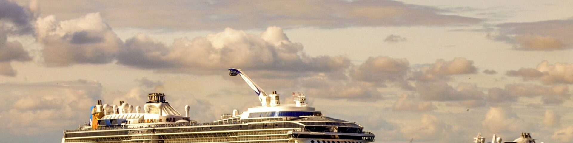 Un gran crucero llamado 'Anthem of the Seas' atracado en un puerto, con otro crucero al fondo.
