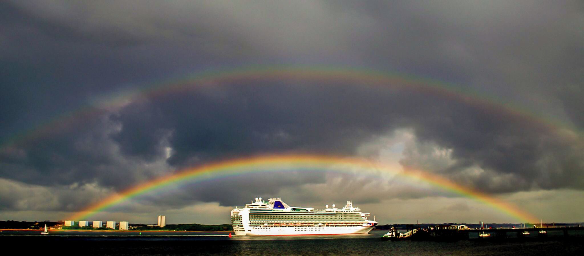A cruise ship with a rainbow in the background.