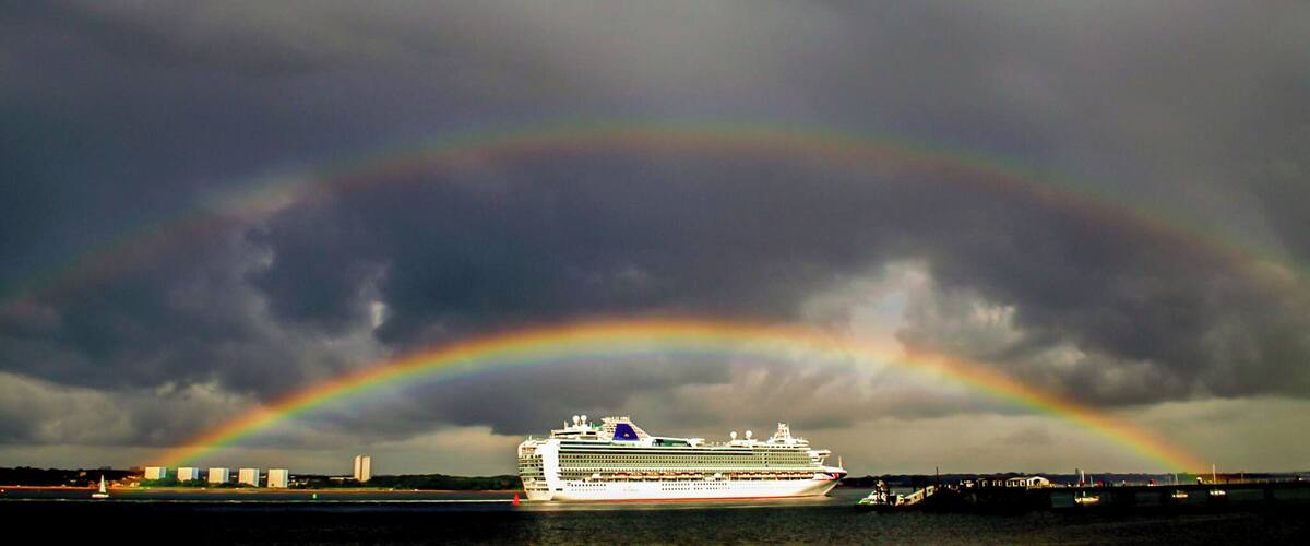 A cruise ship with a rainbow in the background.