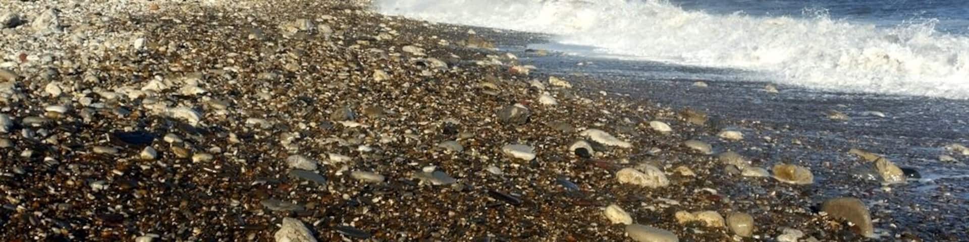 A rocky beach with waves crashing onto the shore and cliffs in the background.