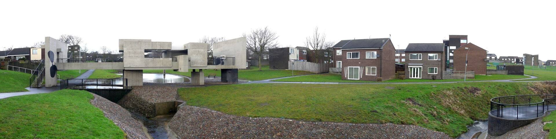 The heart of Peterlee Victor Pasmore's 'Apollo Pavilion' can be seen to the left, crossing the stream, amid a typical residential scene in Peterlee new town, which characteristically includes lots of open space around scattered houses and low level apartment blocks.