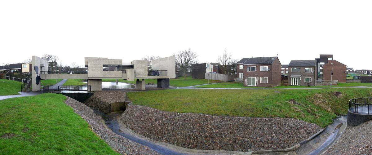 A park with a concrete sculpture, a small stream, and residential buildings.