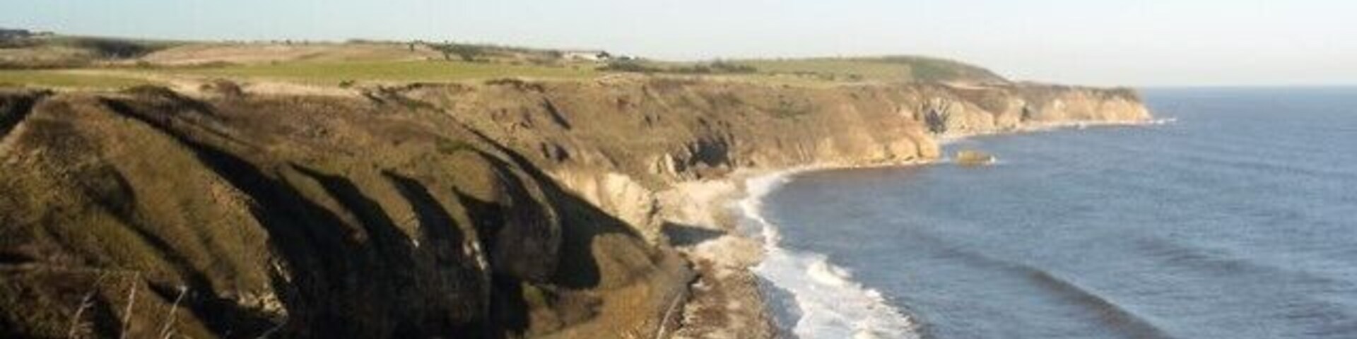 Coast north of Fox Holes from the cliff-top The low, November sun casts long shadows across Easington Beach. The beach ends near the large rock off the headland of Loom with the far headland of Shippersea Point and Beacon Hill visible in the distance.