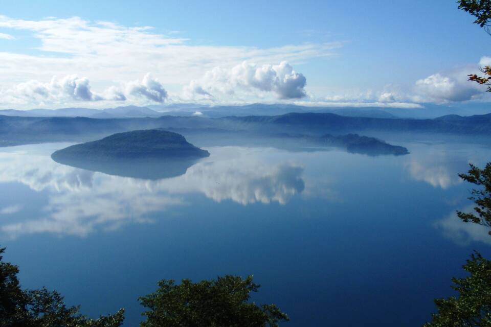 A calm lake with a small island in the center, surrounded by mountains and trees.