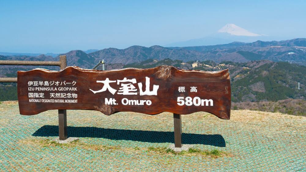 A wooden sign with Japanese text indicating Mt. Omuro at 580m, with a view of mountains in the background.