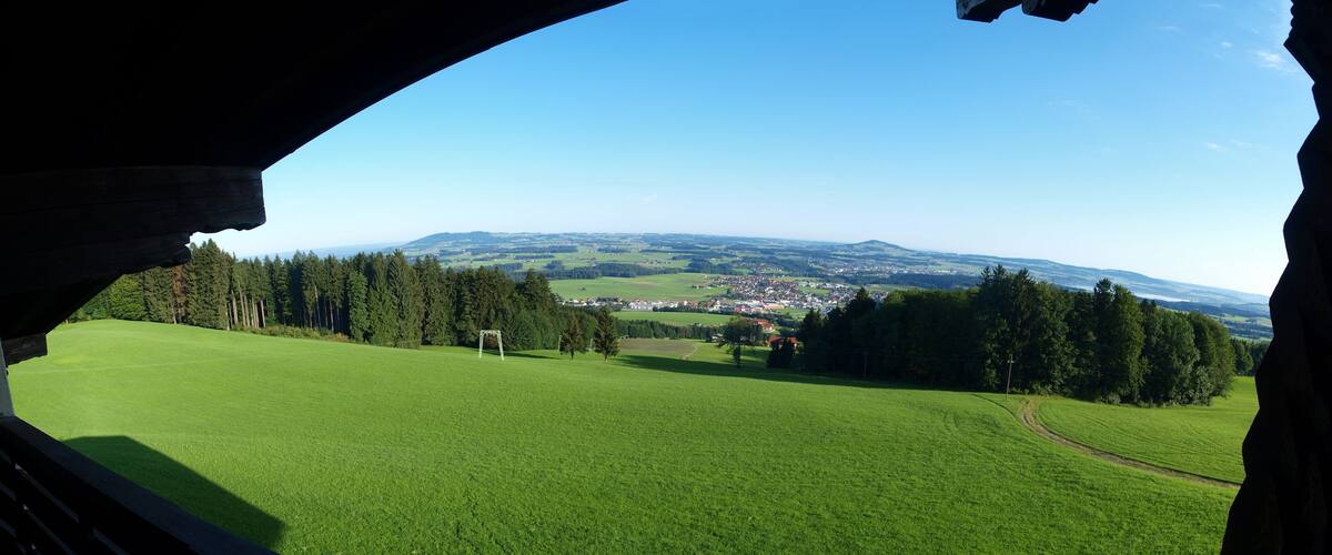 A green field with a town in the distance, surrounded by trees and hills.
