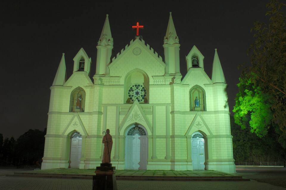 Een kerk in gotische stijl, met een opvallend kruis bovenop, een groot roosvenster en beelden bij de ingang.