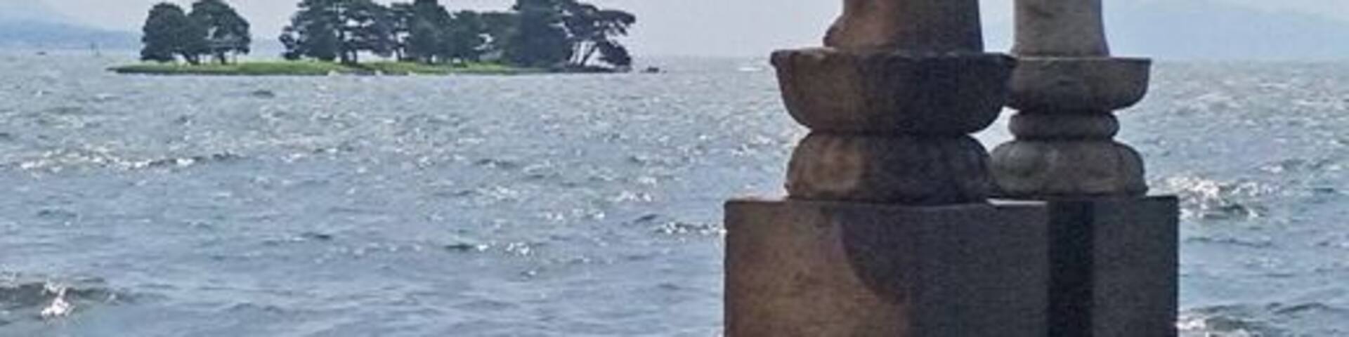 A statue of a figure holding a child, standing on a platform by the sea.