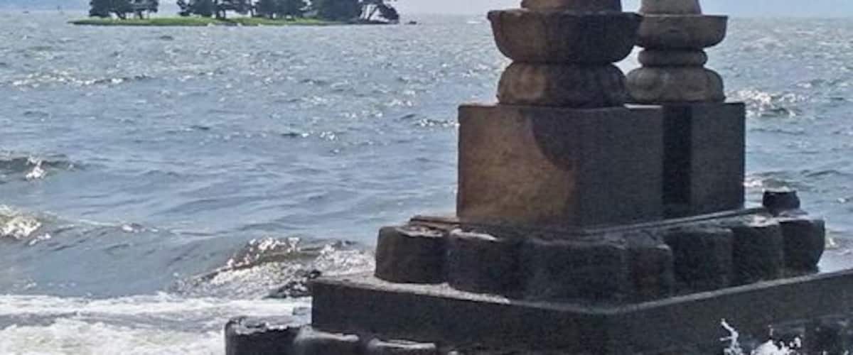 A statue of a figure holding a child, standing on a platform by the sea.