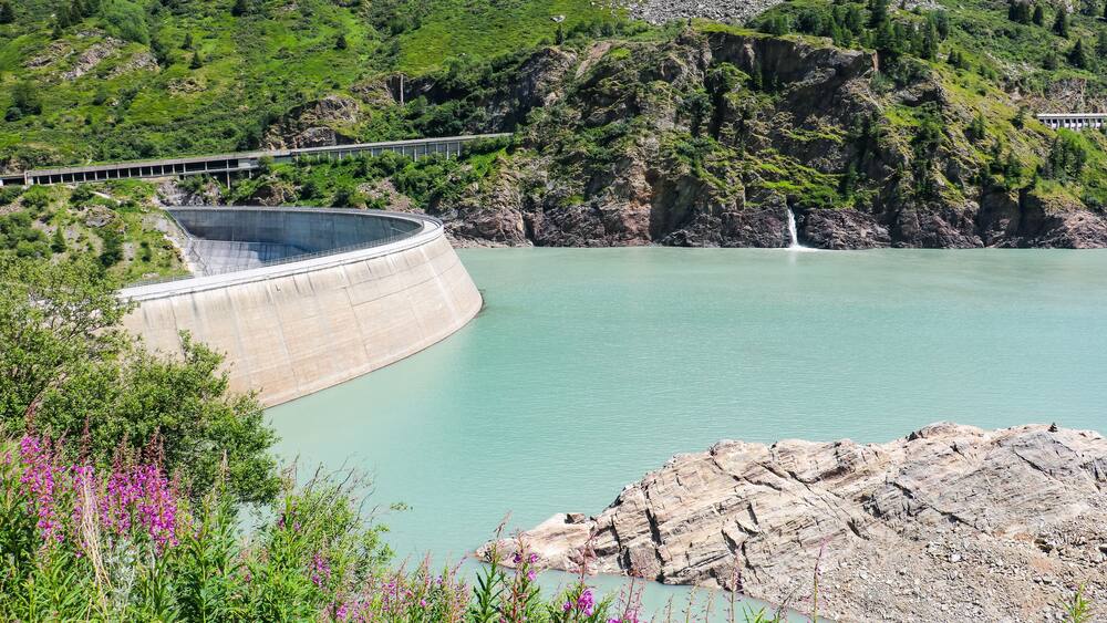 A dam with a bridge, a waterfall, and a lake surrounded by greenery.