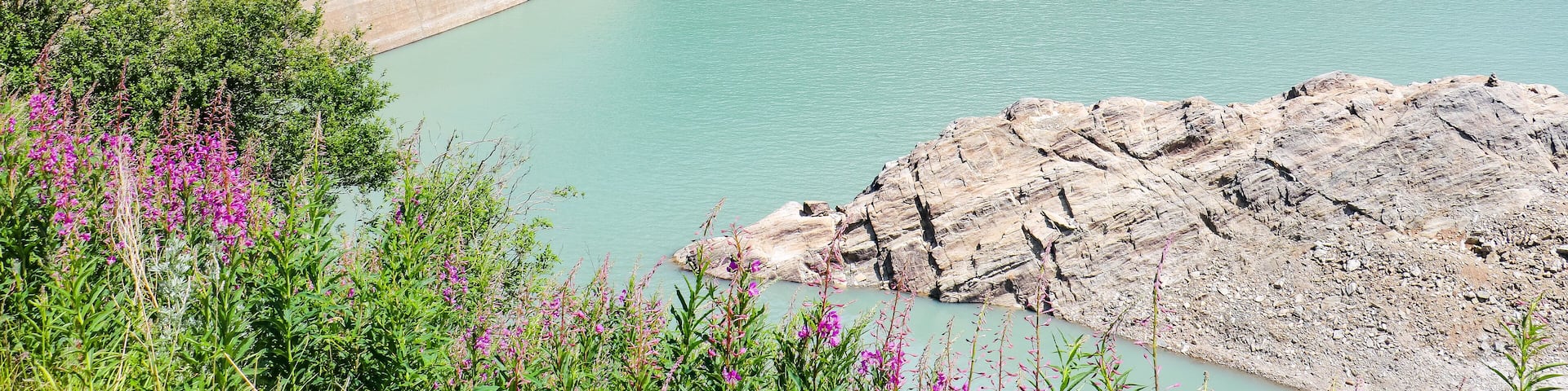 A dam with a bridge, a waterfall, and a lake surrounded by greenery.