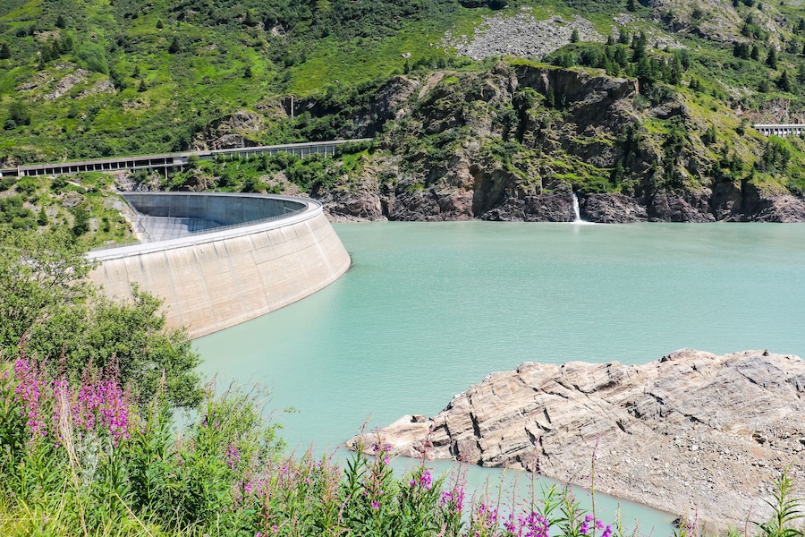 Una presa con un puente, una cascada y un lago rodeado de vegetación.