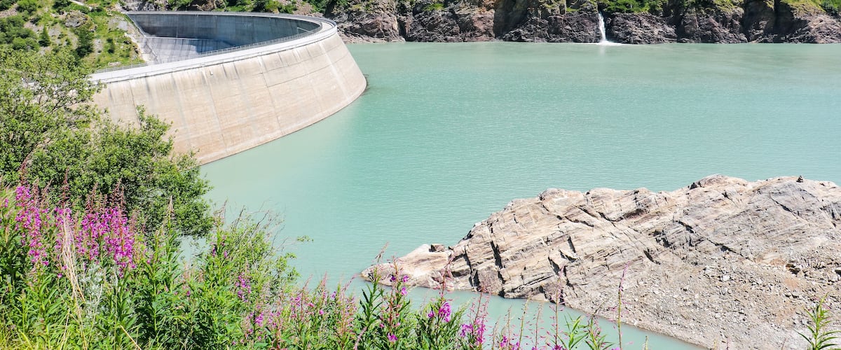 A dam with a bridge, a waterfall, and a lake surrounded by greenery.