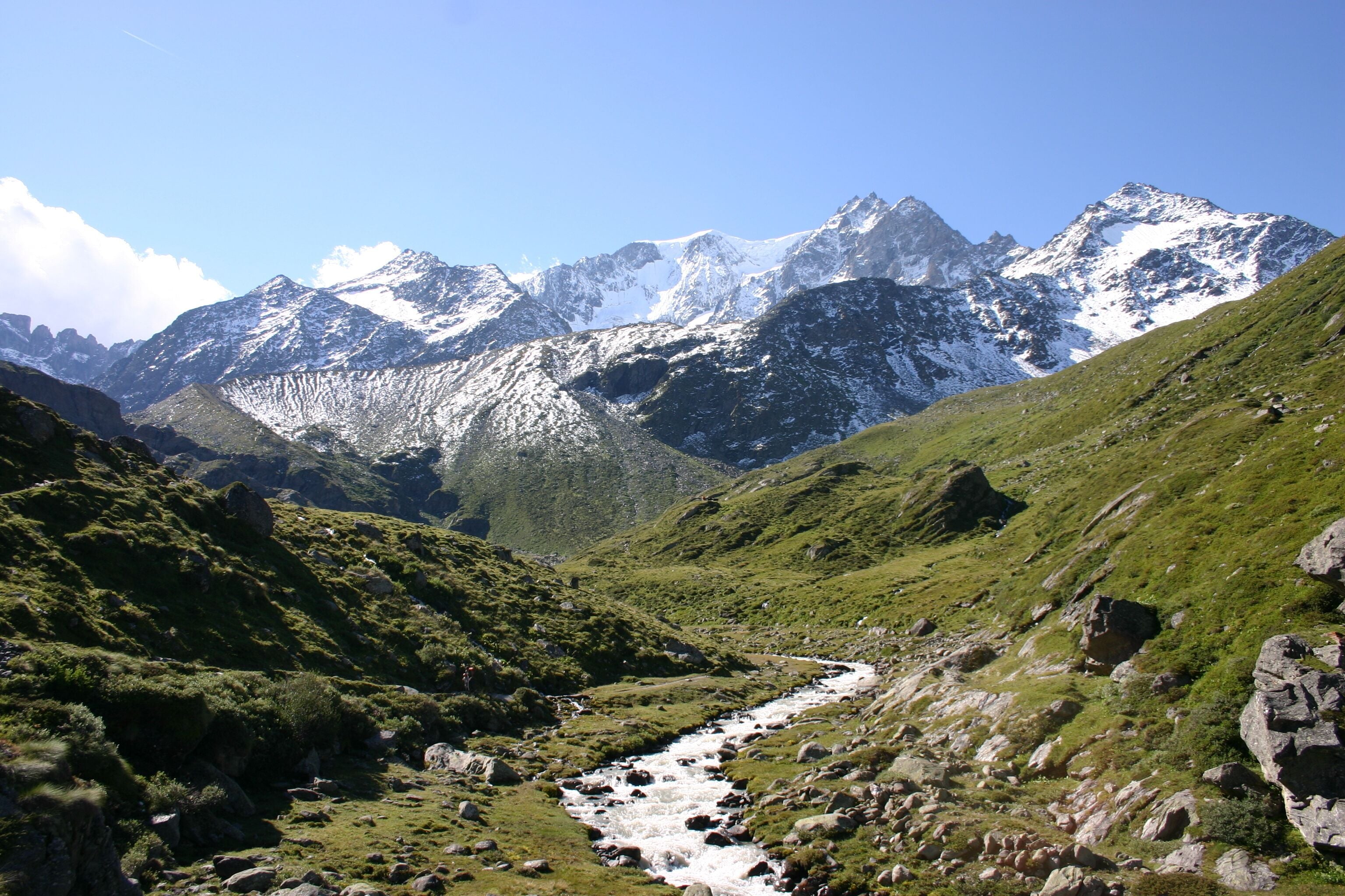 A mountain landscape with a flowing river, rocky terrain, and snow-capped peaks.