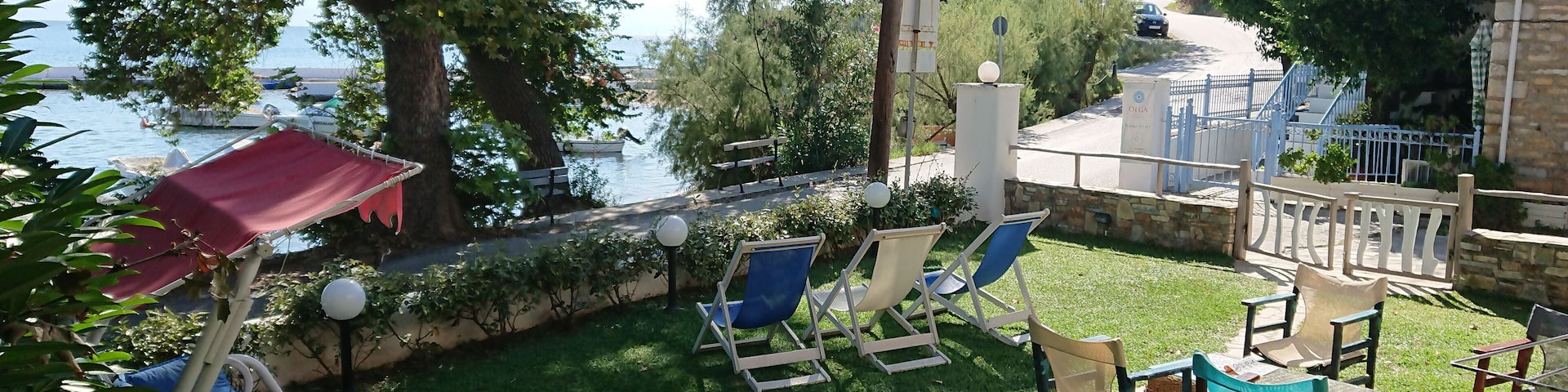 A sunny outdoor seating area with a view of the sea, surrounded by trees and a stone wall.