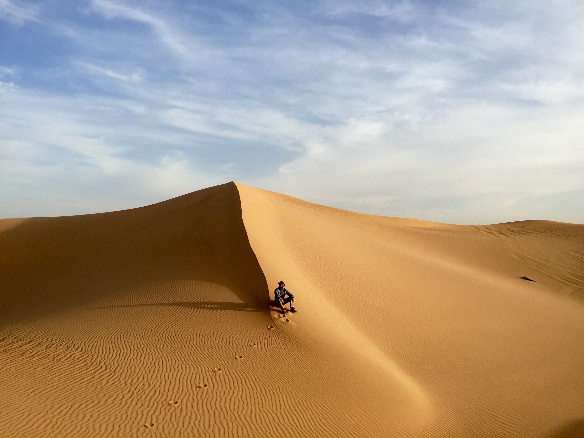 A person sitting on a sand dune in a desert landscape.