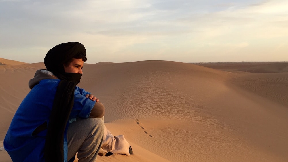 Une personne assise sur une dune de sable, avec un vaste paysage désertique en arrière-plan.