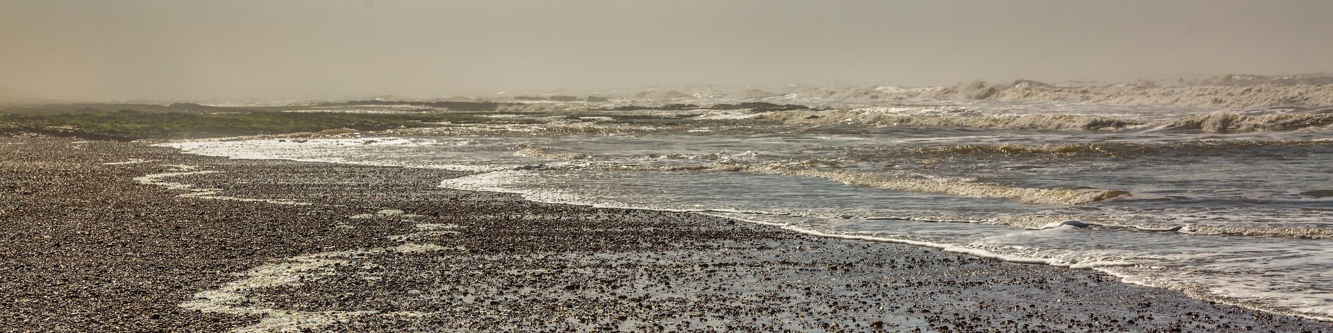 Una playa pedregosa con olas, bajo un cielo nublado.