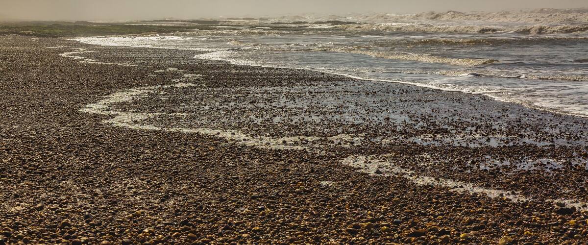 A pebbly beach with waves, under a cloudy sky.