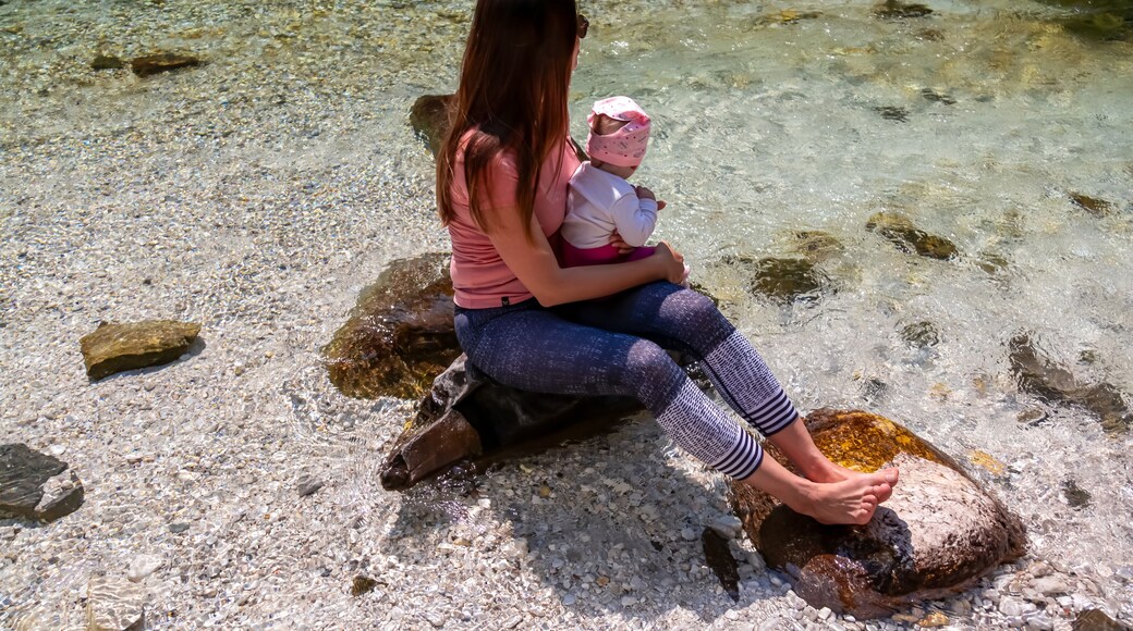 Barefoot woman with baby sitting on rock of Soca River, Bovec, Triglav National Park,Slovenia. Magnificent Soca Valley in Julian Alps. Wanderlust in untamed Slovenian Alps. Hiking in alpine wilderness