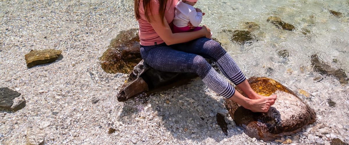 A woman sitting on a rock by a clear stream with pebbles and rocks visible in the water.
