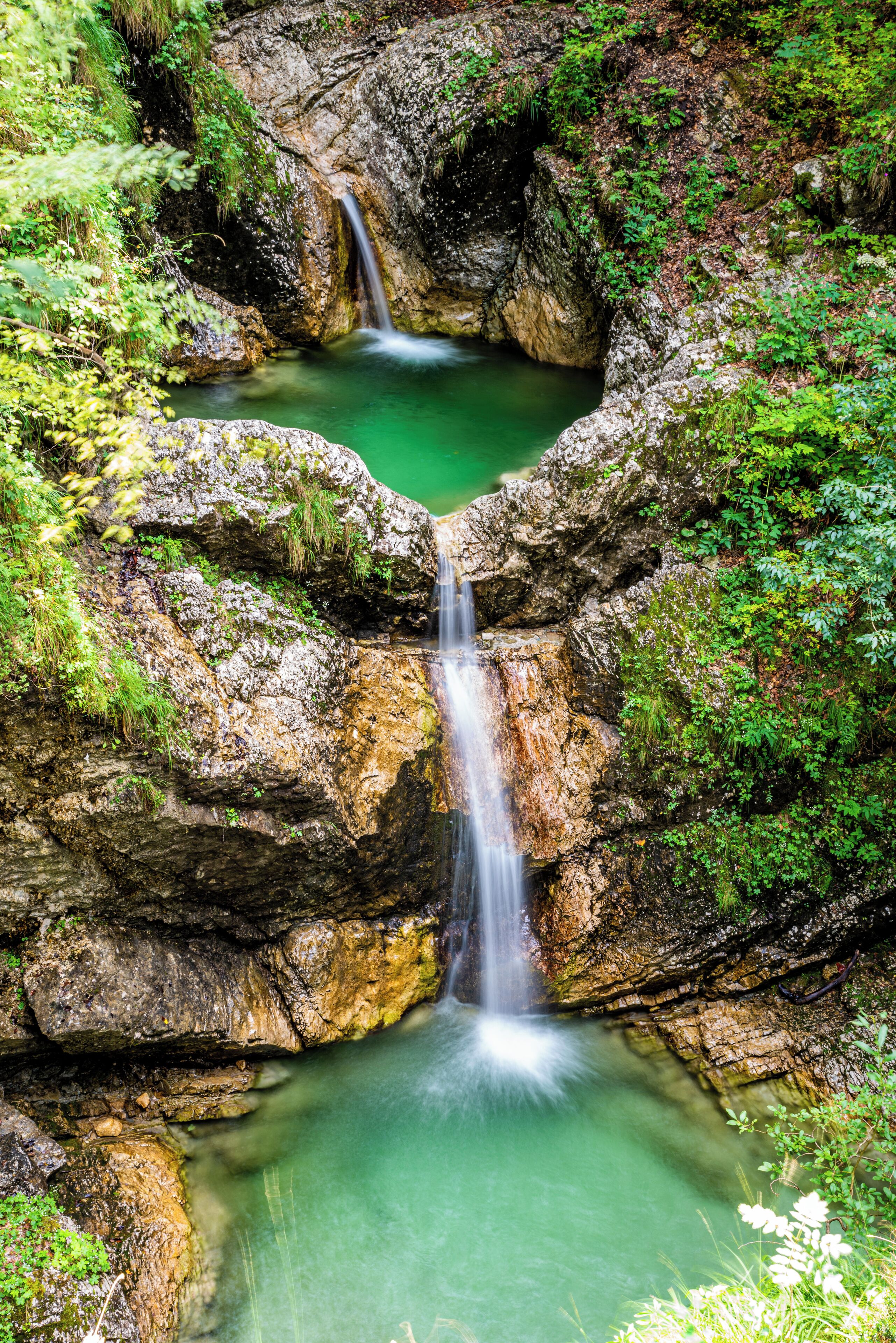 A waterfall cascading into a clear pool surrounded by rocky terrain and lush greenery.