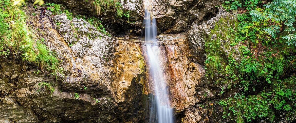 A waterfall cascading into a clear pool surrounded by rocky terrain and lush greenery.