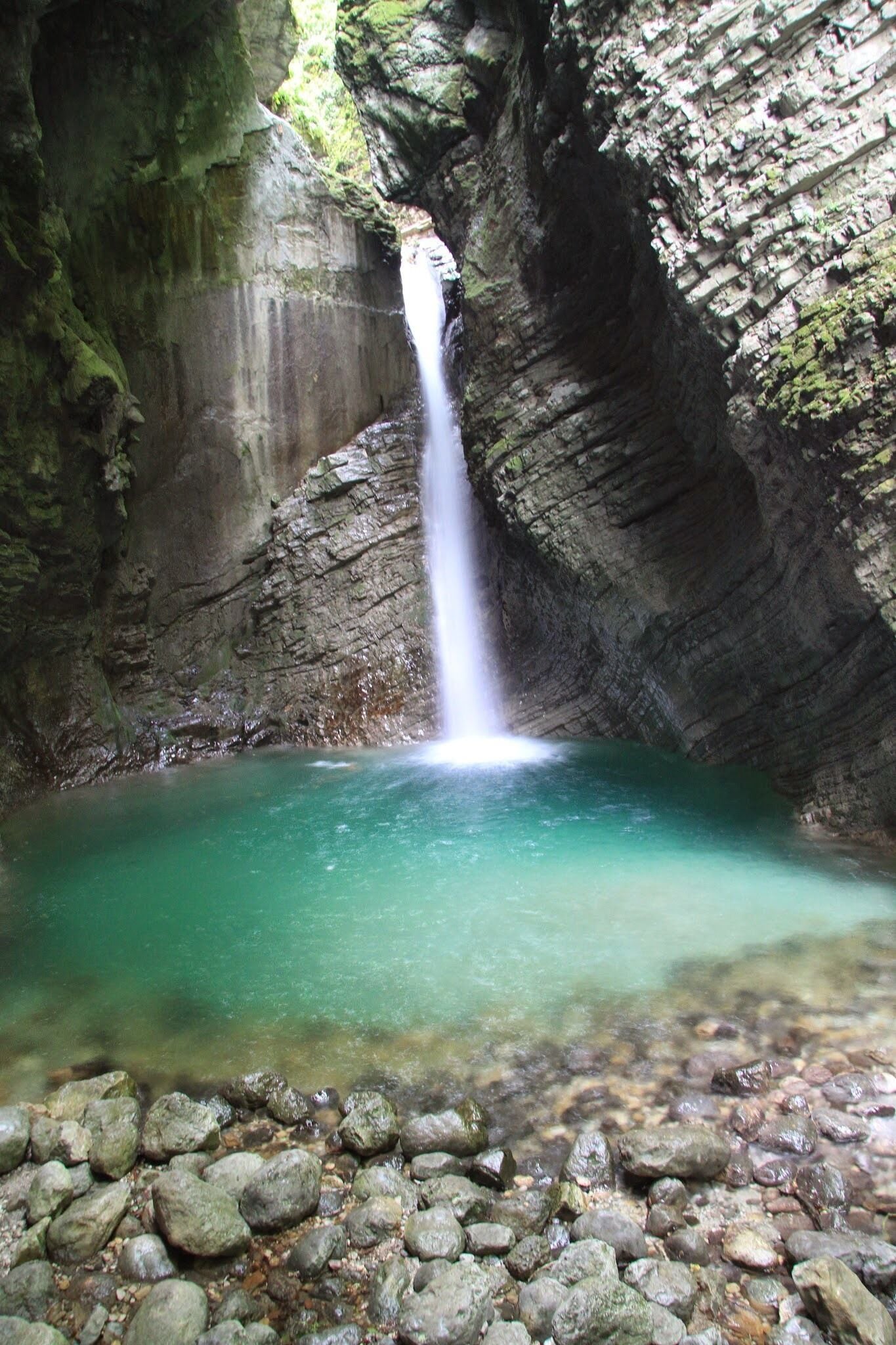 A waterfall cascading into a turquoise pool surrounded by rocky cliffs.