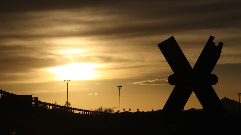 A sunset with a silhouette of a large X-shaped structure against a sky with clouds.