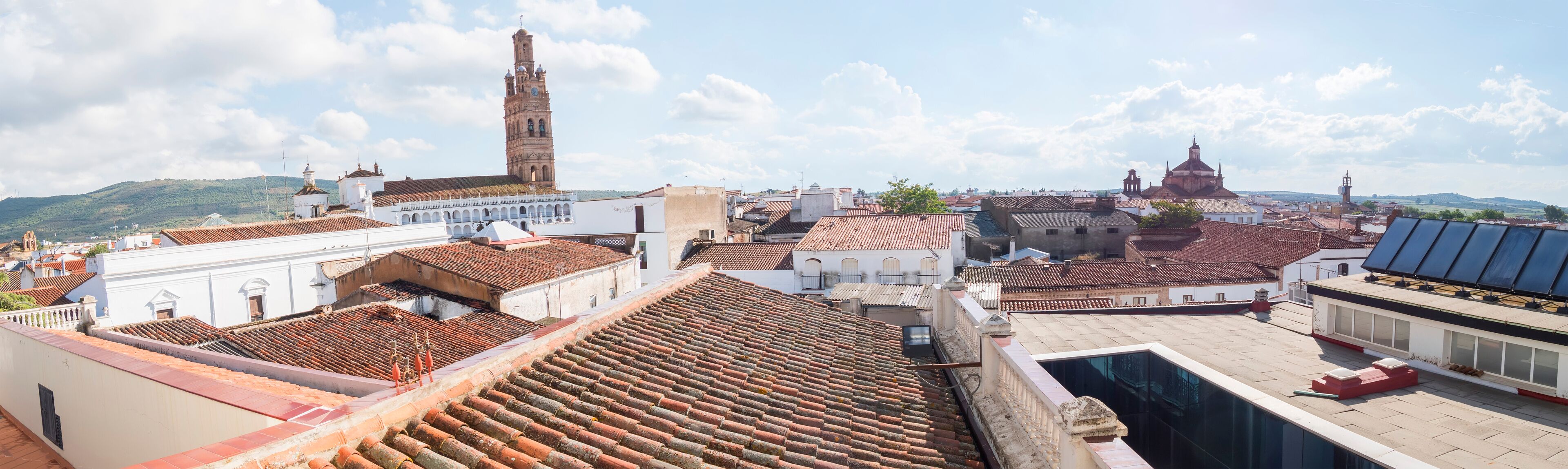 A cityscape with terracotta-tiled rooftops, a prominent church tower, and a mix of historical and modern architecture.