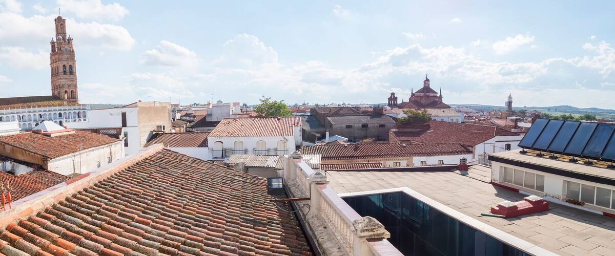 A cityscape with terracotta-tiled rooftops, a prominent church tower, and a mix of historical and modern architecture.