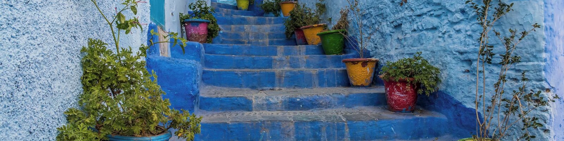 Uma escadaria com vasos suspensos coloridos e uma parede azul.