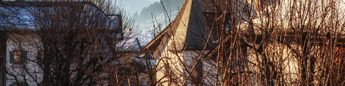 A church with a tall spire, snow-capped mountains in the background, and a clear blue sky.