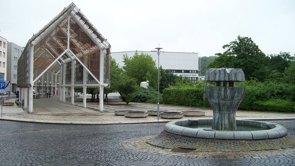 A modern building with a triangular roof, a fountain, and cobblestone pavement.