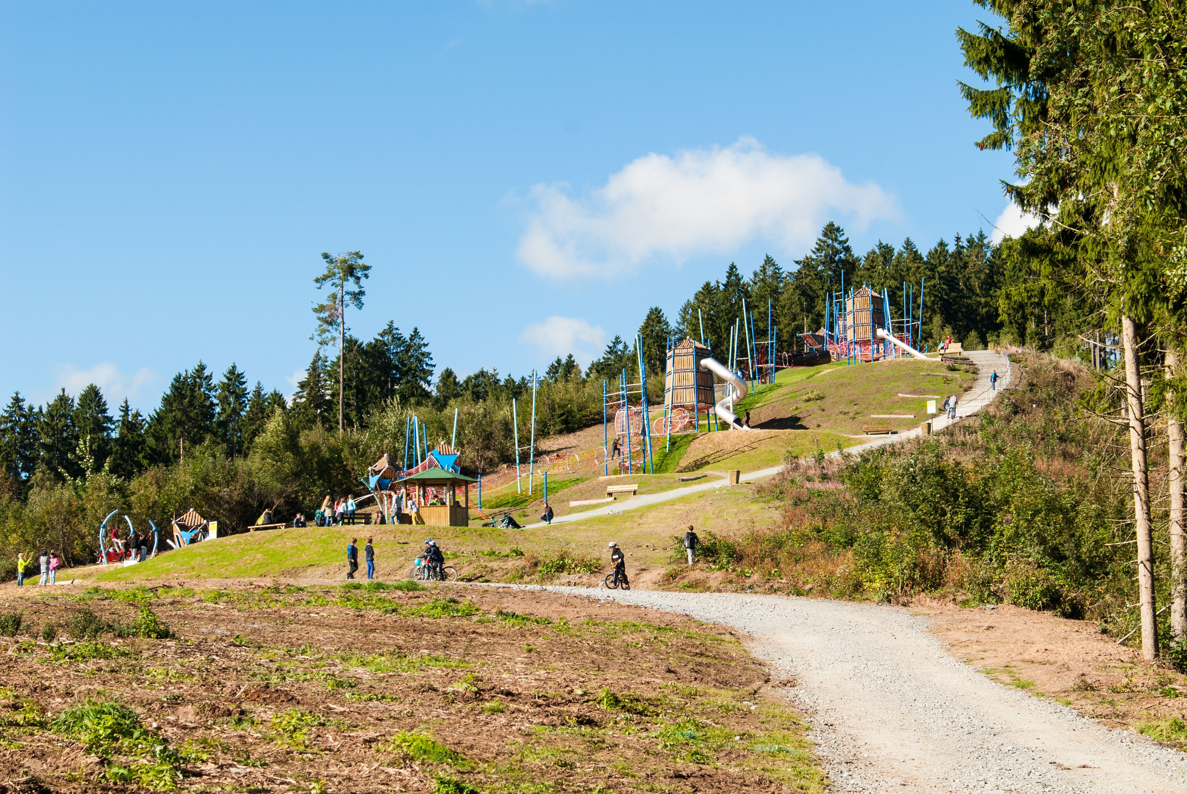 A dirt path leading to a playground with a slide and climbing structures.