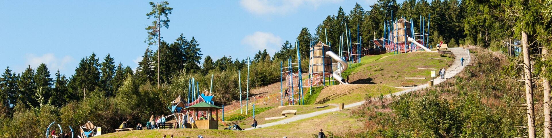 A dirt path leading to a playground with a slide and climbing structures.