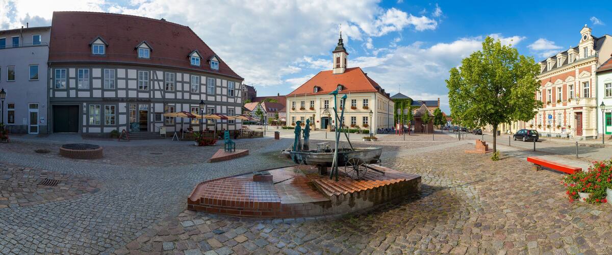 A cobblestone square with historic buildings, a fountain, and a church.
