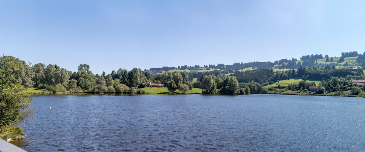 A lake surrounded by hills and trees, with a few buildings in the distance.
