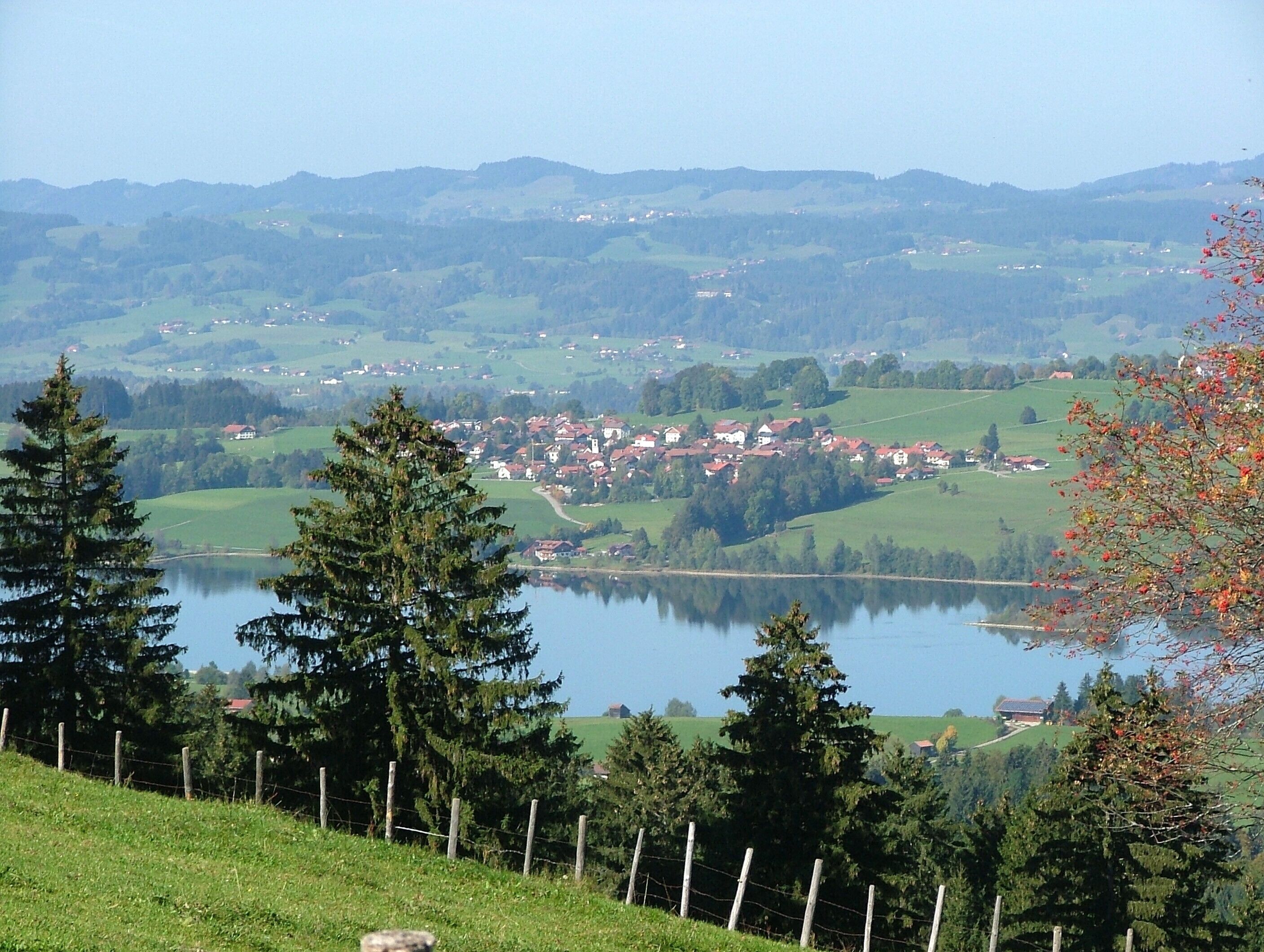 A lake surrounded by a village and forested hills.