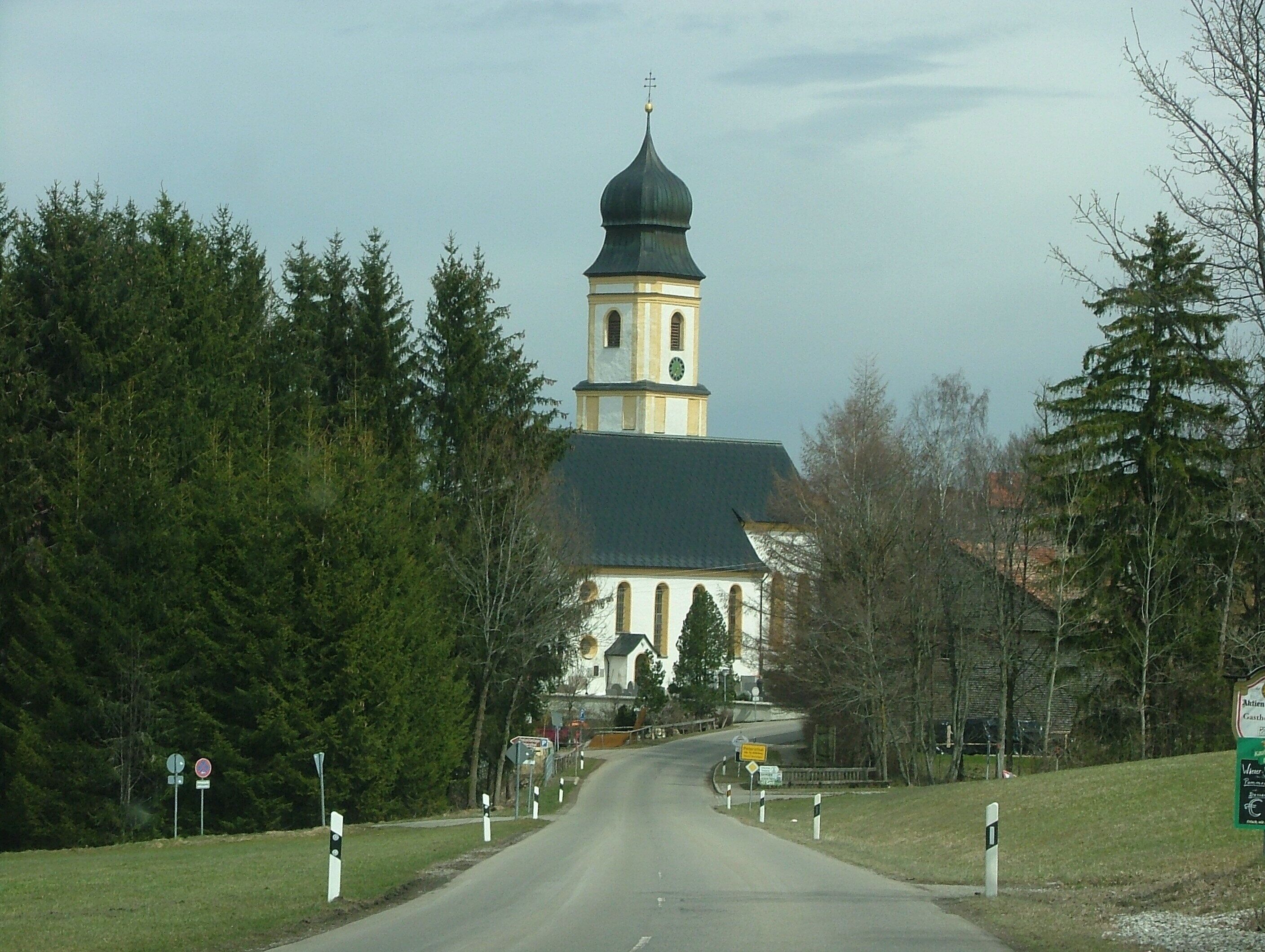 A church with a tall bell tower and a clock, surrounded by trees and a road.