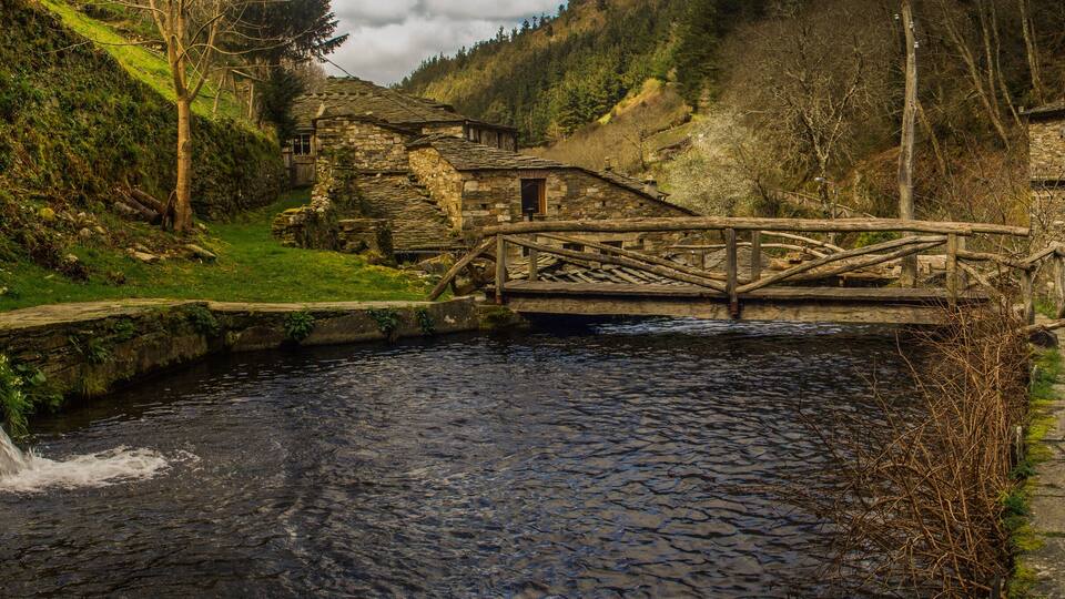 A stone bridge over a river, surrounded by lush greenery and stone buildings.
