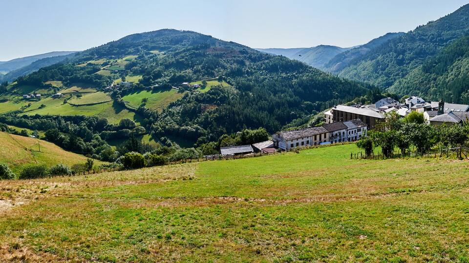 A valley with a small village, green fields, and mountains in the background.